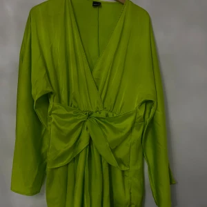 Grön omlottklänning från Glamorous - Snygg grön omlottklänning från Glamorous i storlek L. Klänningen har långa ärmar och en v-ringad design med en stor knytrosett framtill. Perfekt för vårens och sommarens fester!