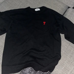 Svart tröja från Ami - Säljer en stilren svart tröja från Ami med ett litet rött hjärta broderat på bröstet. Tröjan är i ett mjukt material och har ribbade muddar vid ärmslut och nederkant. Perfekt för både vardag och fest! 🖤❤️