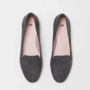 Grå loafers från H&M - Snygga och stilrena grå loafers från H&M.Ett par loafers med ripsband runt kanten. Foder och innersula i satin. Yttersula i gummi. Mörk gråmelerad. Perfekt för vardagligt bruk.