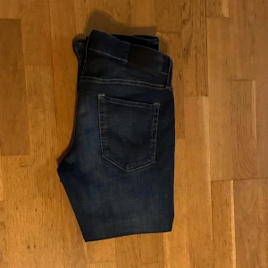 Mörkblå jeans från Jack & Jones - Säljer ett par schyssta mörkblåa jeans från Jack & Jones i modellen Slim Glenn. Det är storlek 31/30, men de är avklippta så de passar en som är 170cm . Byxorna har en klassisk femficksdesign, stretchiga och är i väldigt bra skick. Perfekta för skolan eller gähda!  