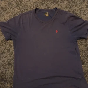 Mörkblå t-shirt från Polo Ralph Lauren - Säljer en snygg mörkblå t-shirt från Polo Ralph Lauren i bomull. Den har en klassisk passform och är kortärmad. Detaljerad med det ikoniska röda broderade märket på bröstet.