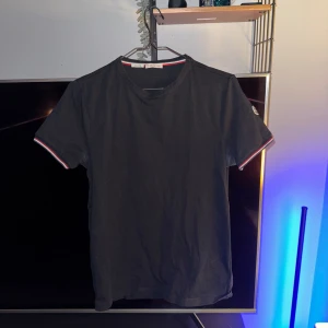 Svart t-shirt från Moncler - Säljer en snygg svart t-shirt från Moncler i bomull. Den har korta ärmar med coola ränder i rött och vitt vid ärmsluten. Perfekt för både vardag och fest! 🖤pris går diskutera 