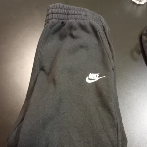 Svarta mjukisbyxor från Nike - Säljer ett par svarta mjukisbyxor från Nike i storlek M(137-147). De är superbekväma med elastisk midja och det klassiska Nike-loggan på benet. Perfekta för chill dagar eller träning. 🖤