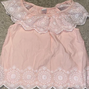 Ljusrosa blus - Den är en off the shoulder blus med vit söming, den är elastisk runt axlarna.