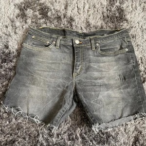 Grå jeansshorts från Davy's - Säljer ett par grå jeansshorts från Davy's i storlek 33. De har en cool vintage-look med slitna kanter och klassisk femficksdesign. Perfekta för en avslappnad sommarstil. Passar både till vardags och festliga tillfällen!