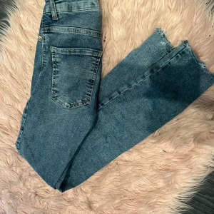 Blå jeans - Säljer ett par snygga blå jeans från gina tricot modell molly. De har en klassisk femficksdesign och är gjorda i ett slitstarkt denimtyg. Jeansen har en fransig kant vid bensluten för en trendig look. Perfekta för vardagsbruk och kan enkelt matchas med olika toppar.