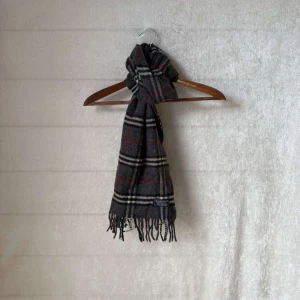 Burberry halsduk - Säljer en klassisk mörk grå halsduk från Burberry. Den är i nyskick. Halsduken är gjord av mjuk 100% lammull. Perfekt för att hålla sig varm under höst och vinter!        Skicket är 9/10 utan defekter och äkta såklart👍