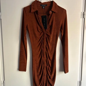 Brun klänning från New yorker  - Snygg brun oanvänd klänning från New yorker i storlek S. Den har långa ärmar och en knäppning framtill med en cool rynkad detalj. Materialet känns mjukt och bekvämt. 💕
