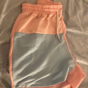 Rosa och blåa shorts med snörning - Snygga och bekväma shorts i rosa och blått med elastisk midja och snörning. Perfekta för en avslappnad dag eller träning. De har en lös passform och är gjorda i ett mjukt material.