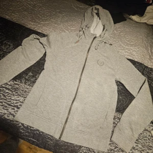 Grå hoodie från North Bend - Säljer en grå hoodie från North Bend med dragkedja och justerbar huva. Perfekt för en avslappnad stil. Den har långa ärmar och är tillverkad i ett mjukt material.