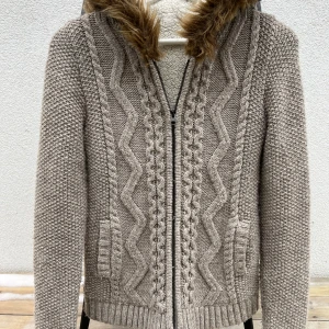 Stickad cardigan  - Mycker trendig mysig grå stickad cardigan med dragkedja och huva med päls. Cardigan har ett snyggt flätmönster framtill och är fodrad med mjuk fleece för extra värme. Perfekt för kyliga dagar!