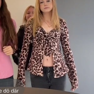 Leopardmönstrad topp med knyt - Snygg leopardmönstrad topp med knyt framtill. Toppen har långa ärmar och en v-ringad design. Perfekt för att ge en djärv touch till din outfit.