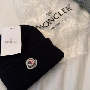 Svart ribbad mössa från Moncler - Snygg svart ribbad mössa från Moncler med broderad logotyp framtill. Perfekt för att hålla värmen under kyliga dagar. Stilren design som passar till det mesta.