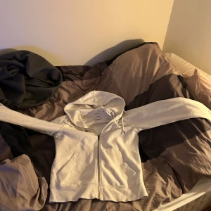 Vit hoodie från Jack & Jones - Säljer en stilren vit hoodie från Jack & Jones. Den har en dragkedja framtill och en praktisk huva med snörning. Perfekt för en avslappnad look.