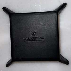 Svart skinnbricka från Palmgrens - Elegant svart skinnbricka från Palmgrens, perfekt för att organisera småsaker. Den har en stilren design med upphöjda kanter och är tillverkad i högkvalitativt skinn. https://www.palmgrens.se/sv/articles/2.48.247/fat-s