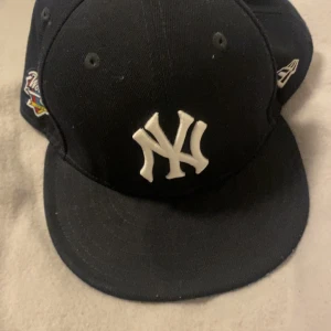 Svart keps med New York Yankees-logga - Snygg svart keps från New Era med New York Yankees-logga framtill. Kepsen har även en World Series-brodyr på sidan och är av modellen 59FIFTY. Perfekt för sportfantasten!