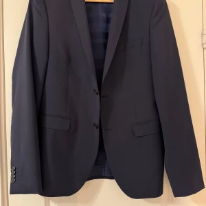 Mörkblå kavaj från s.Oliver Black Label - Elegant mörkblå kavaj från s.Oliver Black Label. Kavajen har en klassisk design med två knappar framtill och fickor med lock. Perfekt för formella tillfällen. Nypris: 1600. 