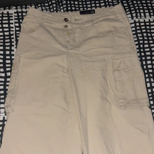 Beige cargobyxor från Kanati - Säljer ett par beige cargobyxor från Kanati med flera praktiska fickor och knappdetaljer. Perfekta för en avslappnad stil med en loose passform. Fungerar perfekt till streetwear då är väldigt flexibla och strechiga.