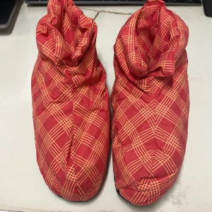 Röda rutiga tofflor - Säljer ett par mysiga röda tofflor med rutigt mönster i gult. Perfekta för att hålla fötterna varma inomhus. De har en mjuk och bekväm sula. Längden: 23.5cm