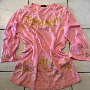 Rosa blus med broderade detaljer - Charmig rosa blus med vackra gula broderier och pärldetaljer. Blusen har långa ärmar och ett luftigt snitt, perfekt för en bohemisk stil. Passar utmärkt för vår och sommar.