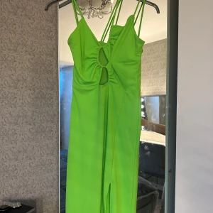 Grön långklänning med cut-out detaljer - Snygg grön långklänning med smala axelband och trendiga cut-out detaljer framtill. Klänningen har en slits som ger extra rörelsefrihet och stil. Perfekt för en somrig look!