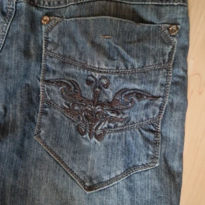 Blå jeans med broderad detalj - Snygga blå jeans med unika broderade detaljer på bakfickan. 