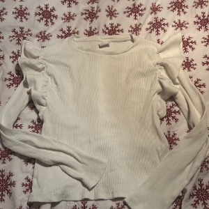 Vit ribbad tröja från Zara - Säljer en stilren vit ribbad tröja från Zara med volangdetaljer på axlarna. Tröjan har långa ärmar och är perfekt för både vardag och speciella tillfällen. Passar barn i storlek 11-12 år. men passar även till dom som har storlek 156 då armarna är stretchiga 