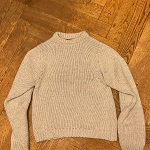 Silvrig stickad tröja från Peak Performance - Säljer en snygg silvrig stickad tröja från Peak Performance. Tröjan är tillverkad av italienskt garn och har en klassisk design med långa ärmar och ribbstickade detaljer vid hals, ärmslut och nederkant. Liten puffärm. Perfekt för kyliga dagar!