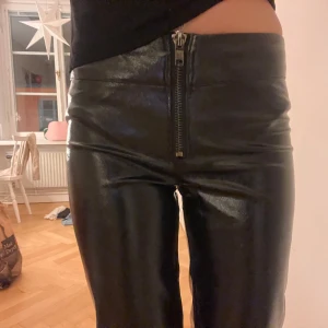  Snygga Svarta skinnbyxor - Snygga svarta skinnbyxor med hög midja och en framträdande dragkedja framtill. Perfekta för en trendig look.