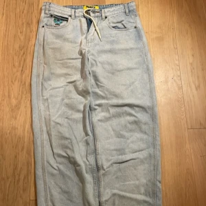 Baggy jeans från Butter - Säljer ett par ljusblå baggy jeans från Butter med coolt broderi av en jordglob på fickan. Jeansen har en avslappnad, baggy passform och är perfekta för en casual look. 30 i waist men har snöre för att minska det. Va inte rädd att ställa frågor om mått eller fler bilder.🙏