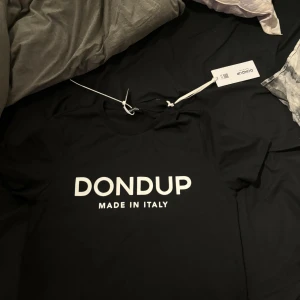 Svart t-shirt från Dondup - Snygg svart t-shirt från Dondup med vit text 'MADE IN ITALY' på framsidan. Perfekt för en stilren och modern look. T-shirten har en klassisk passform och är kortärmad. Den är även helt ny med tag m.m på, säljer den för den var för stor för mig: nypris 999kr 