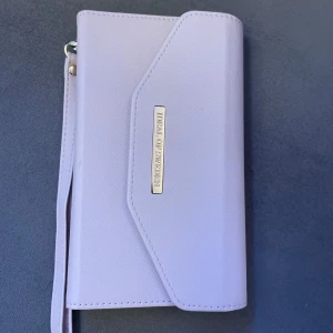 Ljusrosa plånbok med mobilhållare från Ideal of Sweden  - Snygg ljusrosa plånbok från Ideal of Sweden med inbyggd mobilhållare. Plånboken har flera kortfack och en praktisk handledsrem. Perfekt för att hålla ordning på dina kort och mobil på ett stilfullt sätt. Aldrig använd!!