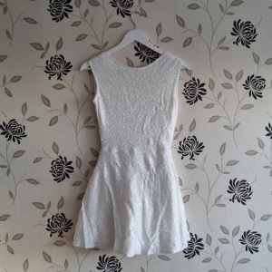 Vit paljettklänning Tobi, Stel: S/36, nyår - Snygg vit klänning med glittrande detaljer och en djup öppen rygg. Den är ärmlös och har en dragkedja bak. Perfekt för en festlig kväll!