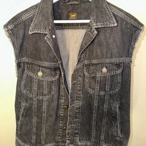 Grå jeansväst från Lee - Snygg grå jeansväst från Lee med fransiga ärmslut och knappar framtill. Västen har två bröstfickor med knappdetaljer och en klassisk krage. Perfekt för en cool och avslappnad stil.nypris 1100kr
