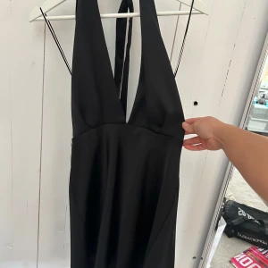 Svart klänning från Zara - Elegant svart klänning från Zara med djup v-ringning och knytband i ryggen. Perfekt för en stilren look.