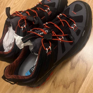 Goretext som är svarta och grå vandringsskor med orange detaljer.  - Snygga och robusta vandringsskor i svart och grått med orange snörning och detaljer. Perfekta för utomhusaktiviteter med bra grepp och stöd.