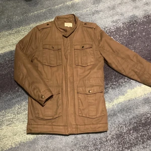 Field jacka - Säljer en olivgrön jacka från Made in the Shade i storlek S. Jackan har en quiltad insida och flera fickor med knappar framtill. Perfekt för vinter, höst eller vår