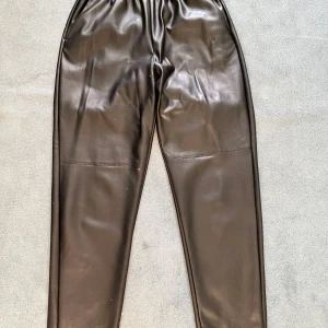 Svarta skinnbyxor med resårmidja - Snygga svarta skinnbyxor med elastisk resårmidja för en bekväm passform. Byxorna har en modern och stilren design, perfekt för att ge din outfit en edgy touch.