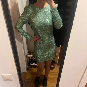 Grön glittrig klänning Mango - Snygg grön glittrig klänning med lång ärm och öppen rygg, storlek S. Perfekt för en festlig kväll. Klänningen har en tight passform och är kort i modellen.