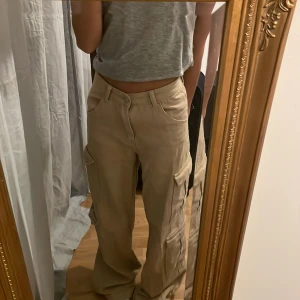 Beige cargobyxor - 💕Säljer ett par snygga beige cargobyxor med hög midja och loose fit. Byxorna har flera praktiska fickor och stängs med dragkedja och knapp. Perfekta för en avslappnad stil. På fjärde bilen ser man en liten fläck som inte gått bort i tvätten, syns inte när man har på sig byxorna då fläcken är på baksidan längre ner💕