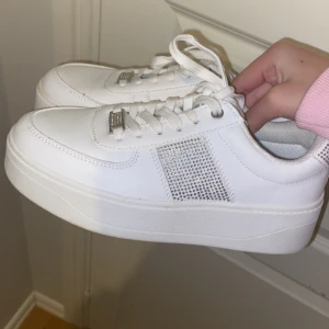 Vita sneakers med glittriga detaljer - Snygga vita sneakers med glittriga detaljer på sidan och hälen. Skorna har snörning. Perfekta för att ge din outfit lite extra bling! Använda 1 gång säljer för att de inte kom till användning inga defekter osäker på vart ja köpte de❤️ (pris kan diskuteras)