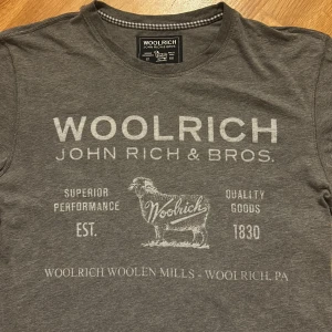 Grå t-shirt från Woolrich - Snygg grå t-shirt från Woolrich med tryck framtill. Den är i mycket bra skick och jag säljer den för endast 299 kr!😊 Hör av er vid minsta fundering! 