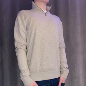 Beige tröja med dragkedja från Jack & Jones - Säljer en stilren beige tröja från Jack & Jones med dragkedja vid halsen. Tröjan har långa ärmar och ribbade muddar vid ärmslut och nederkant. Perfekt för en avslappnad look.