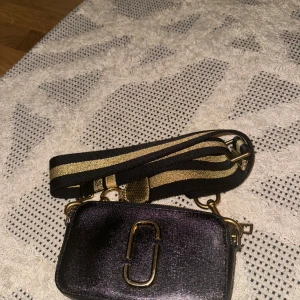 Marc Jakobs bag - Använd men fortfarande en mycket ren och fin väska som inte ser begagnad ut . Väskan medföljer två Marc Jakob band , den ena är den guldiga och den andra har röda detaljer . Väskan är köpt några år sedan så kvitto finns ej .