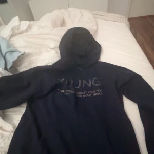 Mörkblå hoodie från Gina Tricot - Säljer en snygg mörkblå hoodie från Gina Tricot med texten 'YOUNG' i glittriga stenar på framsidan. Perfekt för en casual look och superbekväm att ha på sig. Passar perfekt för höst och vinter! Aldrig använd endast testad.