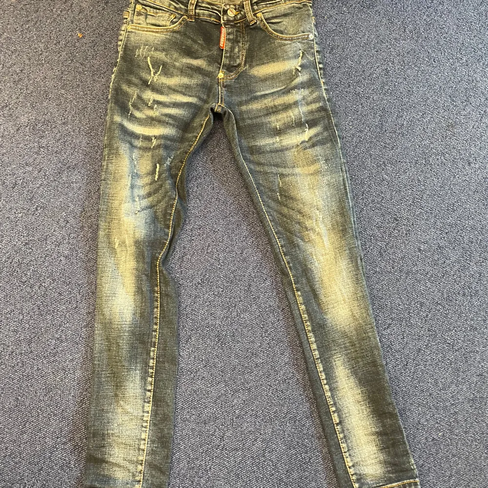 Säljer ett par snygga jeans från Dsquared2. De är blå med en cool slitningseffekt som ger dem en trendig look. Jeansen har en skinny passform och är perfekta för både vardag och fest. De har klassiska fem fickor och en dragkedja framtill.. Jeans & Byxor.