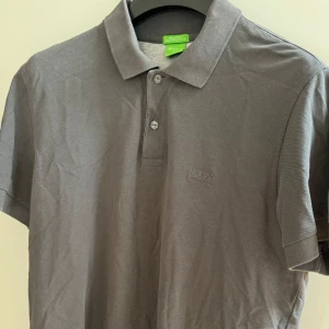 Hugo Boss Piké - Grå Hugo Boss Piké i storlek L. Den är använd men i gott skick och har även kvar extra orginalknappen (se sista bilden). 