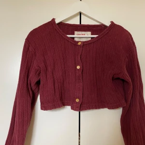 Vinröd croppad kofta - Gullig vinröd kofta i croppad modell, dvs en slags boleroliknande passform. Ribbat material, köpt secondhand och aldrig använd av mig. Passar perfekt för sig själv eller under ett linne/ T-shirt! Storlek L men passar mig som har xs/ s