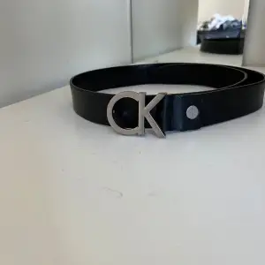 Säljer ett stilrent svart bälte från Calvin Klein. Det har en snygg silverfärgad CK-logga som spänne. Bältet är 90cm långt och är av läder. Nypris 600.