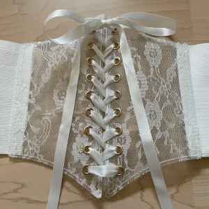 Vit spetskorsett med snörning - Säljer en superfin vit korsett med spetsdetaljer och snörning framtill. Den har guldfärgade knappar och en bred elastisk del som gör att den sitter bekvämt! 💖